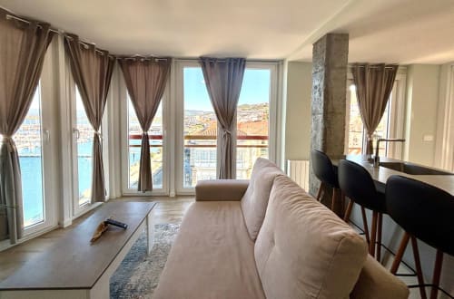 Moderno salón de apartamento con vistas al mar de Baiona, España. Sofá beige, ventanales con cortinas, barra