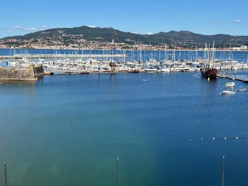 Marina de Baiona con veleros, aguas azules y pueblo en la ladera para apartamento solo adultos Holibai