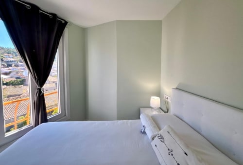 Dormitorio moderno en  Baiona con balcón vista al mar, cama blanca y vistas panorámicas de la ciudad