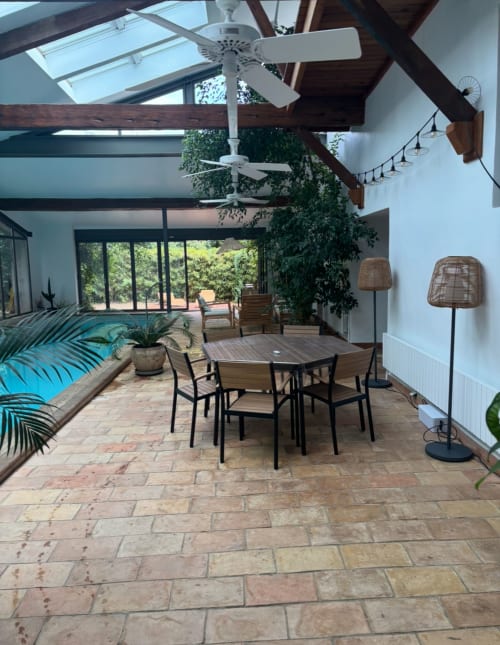 Modern villa interior at La Conciergerie De Franck with dining table, ceiling fans, skylights, and pool view through glass