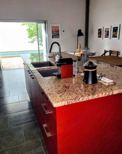 Modern kitchen with red island, granite countertop, and pool view at La Conciergerie De Franck villa in Boissieres