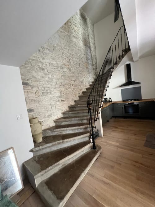 Modern open-plan living area with stone staircase, black railing, wooden flooring, and kitchen in La Conciergerie De Franck