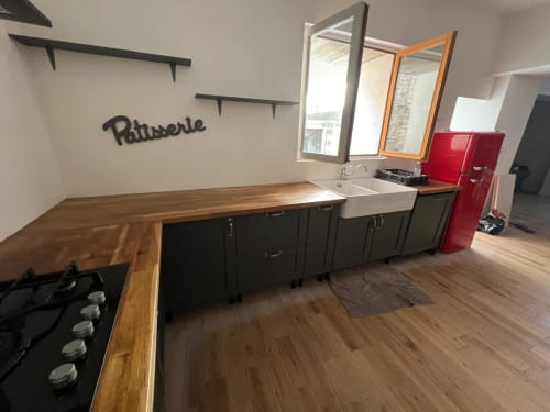 Modern kitchen with wooden countertop, black cabinetry, gas stove, sink, red refrigerator, mirrors, and shelves at La