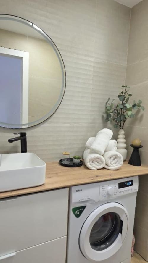 Baño moderno con espejo redondo, lavabo blanco y lavadora en el apartamento MiramaRent, Benicàssim