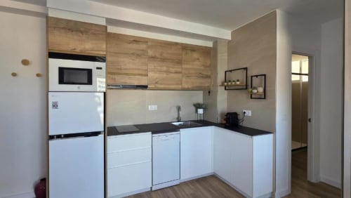 Cocina moderna con muebles de madera y blancos, encimera negra, microondas, refrigerador y fregadero en apartamento de Benicàssim