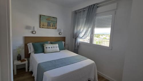 Habitación luminosa con balcón con vistas al mar en MiramaRent, Benicàssim. Cama de madera con detalles en verde azulado, ventana con vista al mar, diseño moderno