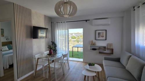 Moderno salón de apartamento con vista al mar y balcón en Benicàssim, incluyendo zona de comedor, sofá y puertas de cristal hacia el océano