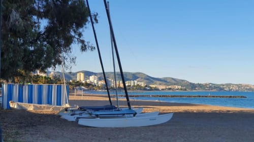 Playa de Benicàssim con veleros y caseta de almacenamiento azul, vistas al Mediterráneo con montañas y pueblo costero