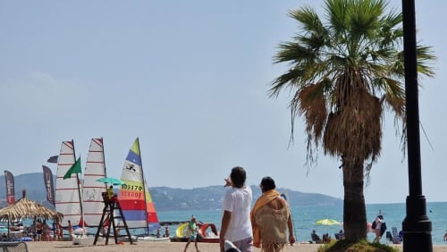 Playa de Benicàssim con tablas de windsurf, palmera y vistas al mar Mediterráneo desde el apartamento MiramaRent