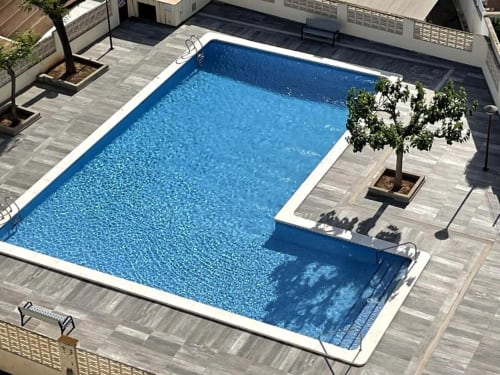 Vista aérea de la piscina rectangular de MiramaRent con borde blanco, terraza de madera gris y árbol en Benicàssim