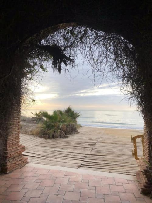 Puerta arqueada de ladrillo que abre a una terraza de madera con vistas al mar en el Apartamento Regata, Benicàssim