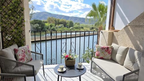 Balcón del Apartamento Regata con barandilla de hierro forjado con vistas al lago de Benicàssim, amueblado con asientos de mimbre y flores rosas