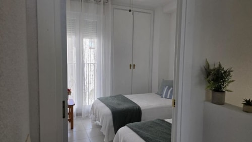Dormitorio luminoso en el apartamento Regata en Benicàssim con dos camas, armarios blancos, plantas en maceta y luz natural