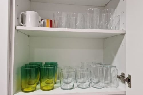 Armario de cocina organizado con vasos transparentes, tazas ombré verde, jarra blanca y taza rayada en villa