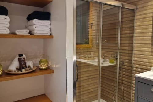 Baño moderno con ducha de estilo madera, toallas blancas dobladas en estantes y amenidades spa en villa de Benicàssim