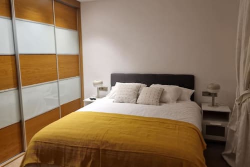 Dormitorio de villa moderna en Benicàssim con cama queen, manta amarilla, armario de madera y blanco, mesitas de noche y paredes beige