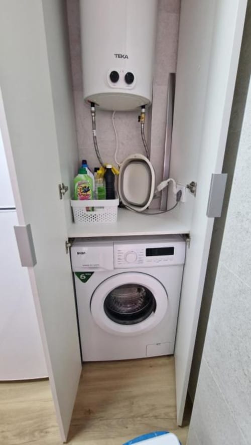 Pequeño armario de lavandería con lavadora blanca apilada y calentador de agua TEKA en apartamento de Benicàssim