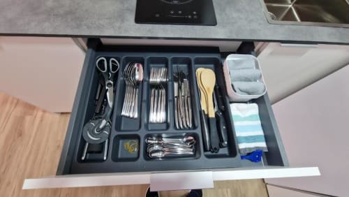 Cajón de utensilios organizados con cubertería, tijeras y herramientas de cocina en apartamento frente al mar