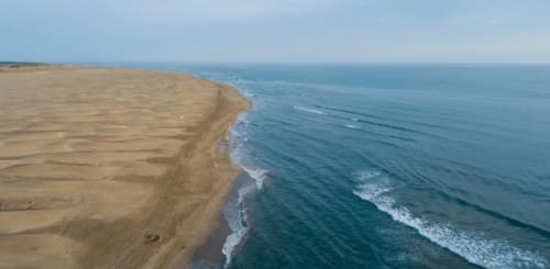 Coastal sandy beach with ocean waves at Boissieres, France. Aerial view of shoreline meeting blue sea.