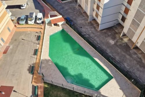 Vista aérea de la piscina verde del apartamento MiramaRent en Benicàssim con patio y edificios circundantes