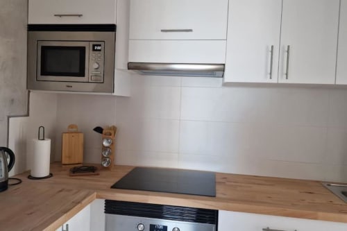 Cocina moderna con vista al mar en apartamento de MiramaRent: gabinetes blancos, encimera de madera, microondas empotrado y acero inoxidable