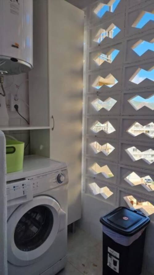 Lavadero del apartamento de Benicàssim con lavadora y vista al océano a través de paneles decorativos de ventana