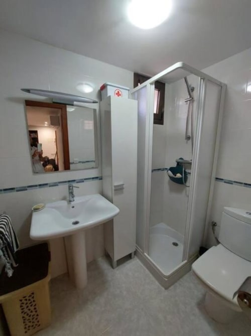 Baño moderno en apartamento MiramaRent, Benicàssim con azulejos blancos, lavabo de pedestal, ducha cerrada, inodoro y espejo