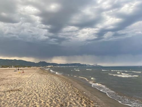 Playa de arena en Benicàssim con olas, montañas al fondo y cielo mediterráneo nublado