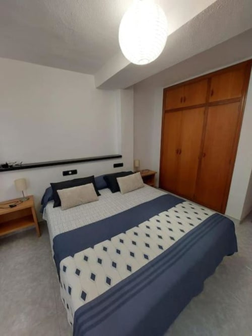 Dormitorio moderno en apartamento de Benicàssim con cama queen, armario de madera y lámpara de techo