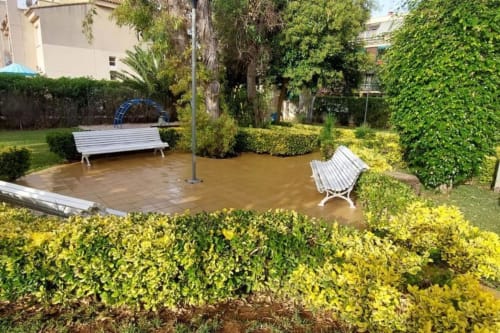Patio de jardín anegado en el apartamento MiramaRent en Benicàssim con bancos blancos y exuberantes setos verdes