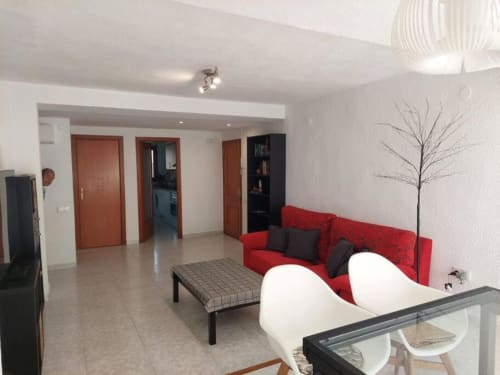 Sala de estar moderna con sofá rojo, sillas blancas y vista al jardín en Benicàssim, España