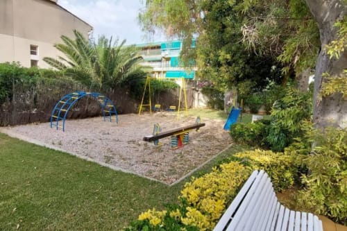 Parque infantil en el apartamento MiramaRent en Benicàssim con arco de escalada, columpio, balancín y tobogán rodeados de árboles
