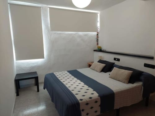Dormitorio moderno con cama doble, cabecera negra, ropa de cama estampada y ventana iluminada en el apartamento MiramaRent