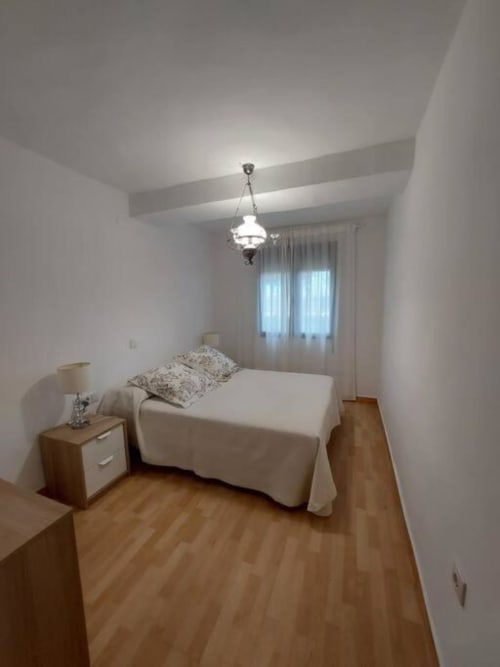 Dormitorio luminoso en apartamento MiramaRent, Benicàssim con cama, mesilla, lámpara colgante y vistas al jardín