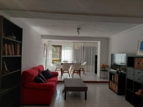 Salón moderno con sofá rojo, zona de comedor, televisión y puertas con vistas al jardín en Benicàssim
