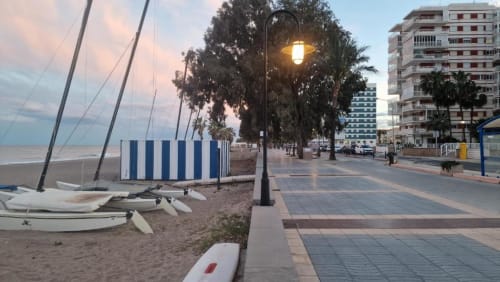 Paseo marítimo en Benicàssim al atardecer con veleros, palmeras y edificios residenciales frente al mar al anochecer