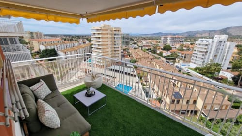 Terraza de apartamento al atardecer en Benicàssim con balcón amueblado, césped artificial, toldo amarillo y vistas panorámicas de la costa