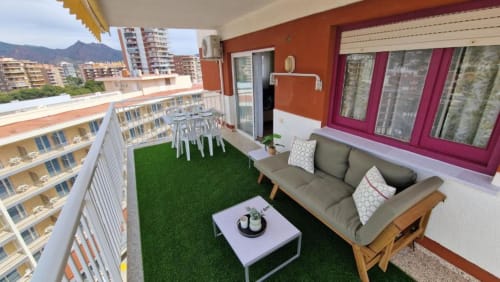 Terraza moderna de apartamento en Benicàssim con césped artificial, sofá gris, mesa blanca y vistas a las montañas