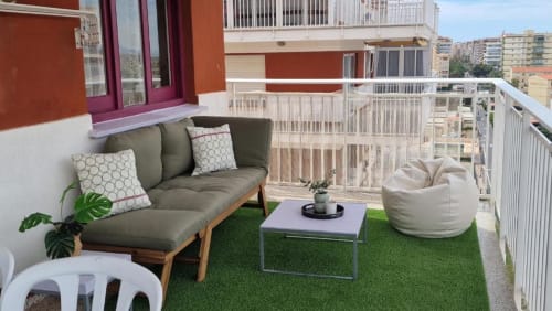 Terraza moderna con césped artificial verde, sofá gris, puf y vistas al océano en el apartamento Sunset de MiramaRent