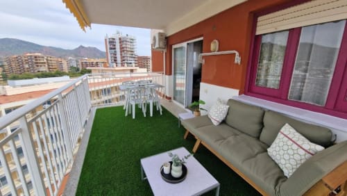 Terraza de apartamento en Benicàssim con césped artificial, sofá gris, zona de comedor, vistas a la montaña y el mar