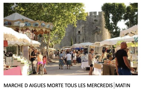 Aigues-Morte market day with medieval tower, vendor stalls, carousel, and visitors in Boissières