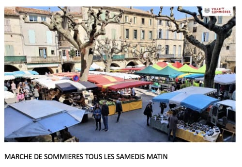 Sommières Saturday morning market with colorful vendor tents and historic buildings, near La Conciergerie De Franck hotel