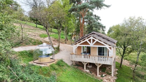 Lodge in legno con spa presso Cabanes et lodges du Belvédère a Serrières-sur-Ain, circondato da alberi e colline.