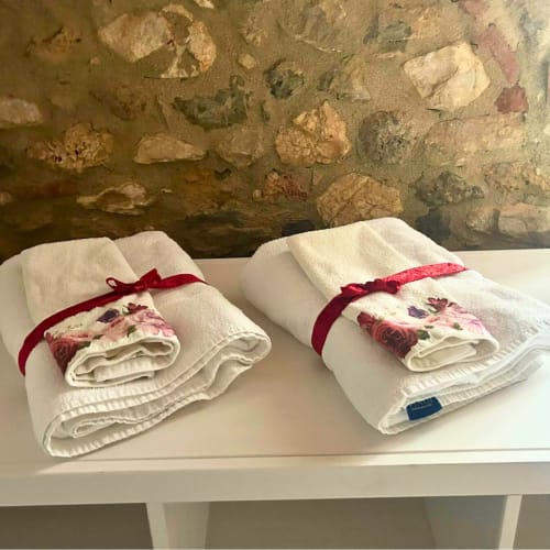 Asciugamani bianchi arrotolati con nastri rossi e dettagli floreali esposti su mensola bianca presso B&B Torre Della Chiocciola, Monteriggioni