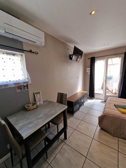 Coin repas du studio Le Loup à Lamotte-Beuvron avec table moderne, chaises confortables, climatisation et télévision, donnant accès direct à la terrasse privée pour un séjour agréable en Sologne.