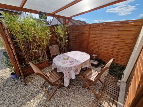 "Terrasse semi-couverte du studio Le Loup à Lamotte-Beuvron, avec table de jardin, chaises en bois et coin détente intime entouré de bambous et palissade en bois, idéale pour un séjour en Sologne."