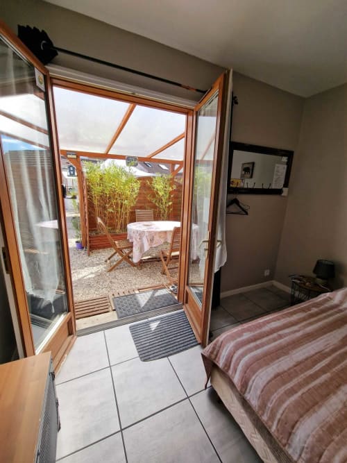 Vue depuis la chambre du studio Le Loup à Lamotte-Beuvron donnant sur la terrasse semi-couverte avec table et chaises en bois, idéale pour un séjour agréable en Sologne
