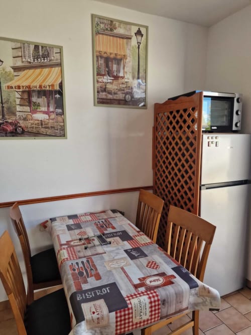 Coin repas du gîte Harmonie à Lamotte-Beuvron avec table bistrot conviviale, chaises en bois, réfrigérateur et four, ambiance chaleureuse idéale pour un séjour en Sologne.