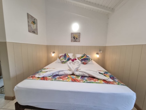 Bright studio bedroom at Gites Kaladja with double bed, colorful tropical bedding, beadboard walls, and modern amenities