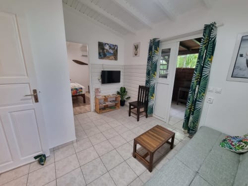 Lewoz apartment living room at Gites Kaladja in Port-Louis with tropical décor, TV, wooden furniture and pool view doors